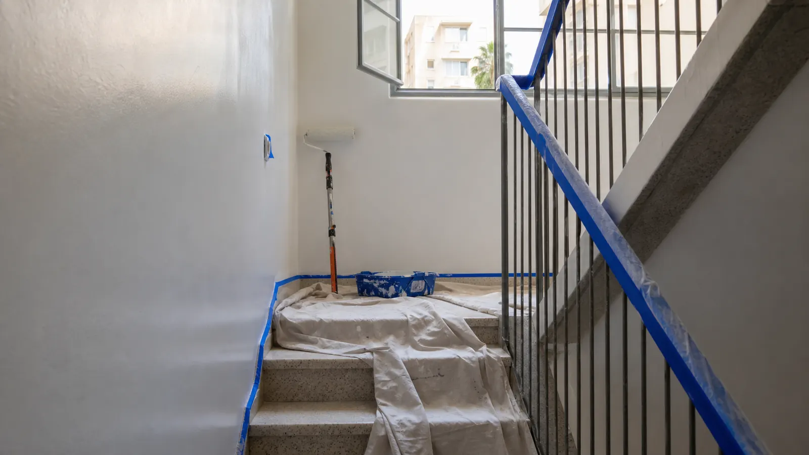 חדר מדרגות באמצע צביעה — קירות טריים, כיסוי על המדרגות וגלגלת על פודסט